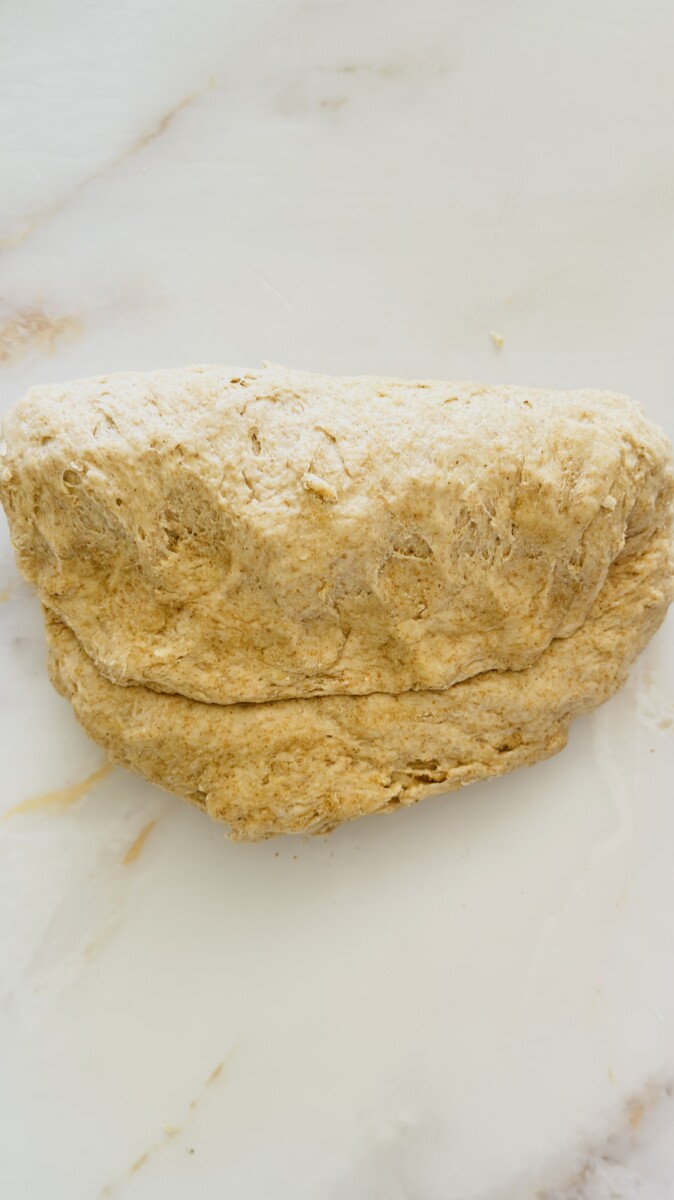 Beginning to knead pita bread dough by folding it in half on a floured surface.