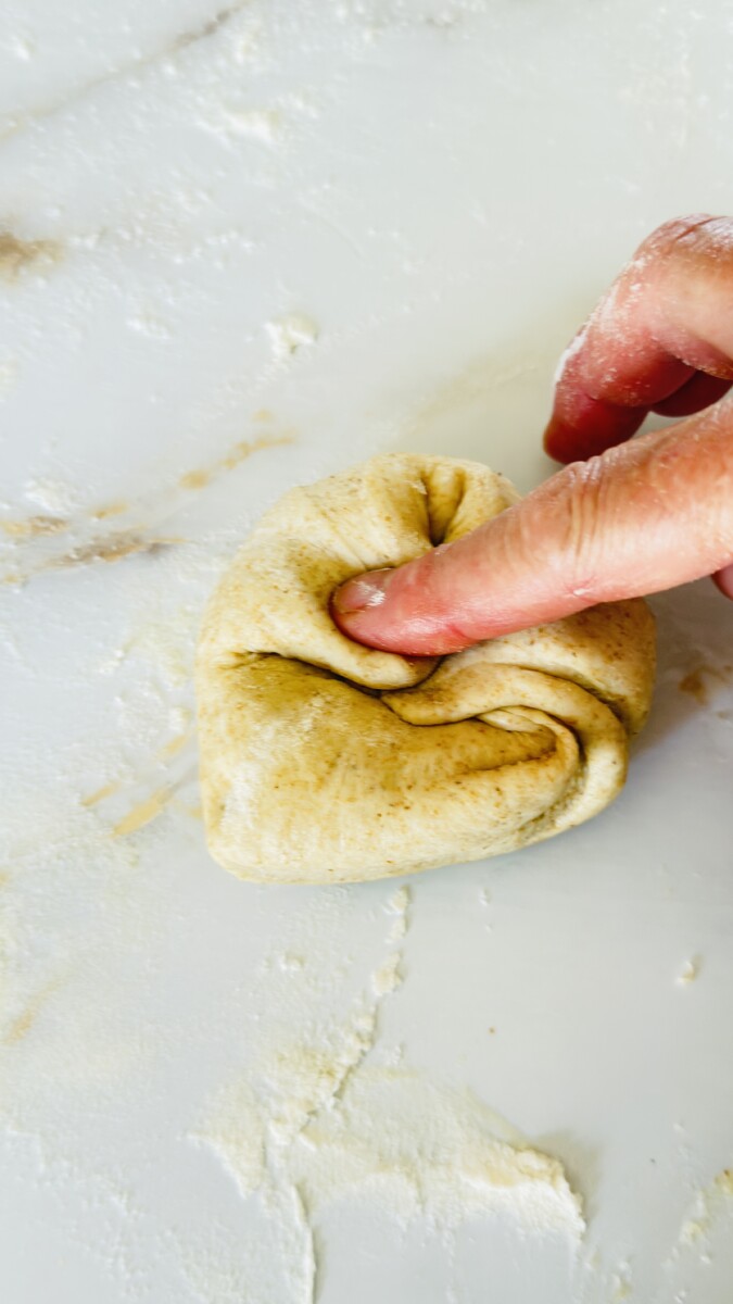 Folding the second corner of the dough triangle toward the center while shaping pita bread.