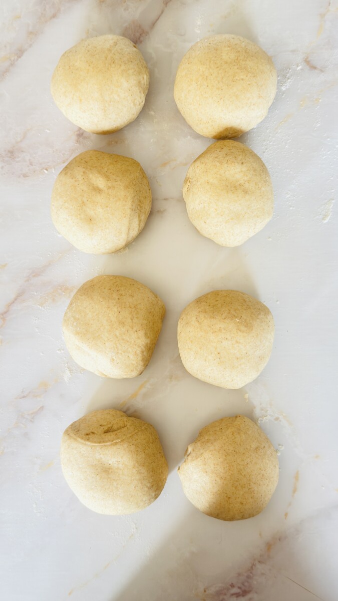 Eight round pita bread dough balls resting on the counter, covered, before rolling.