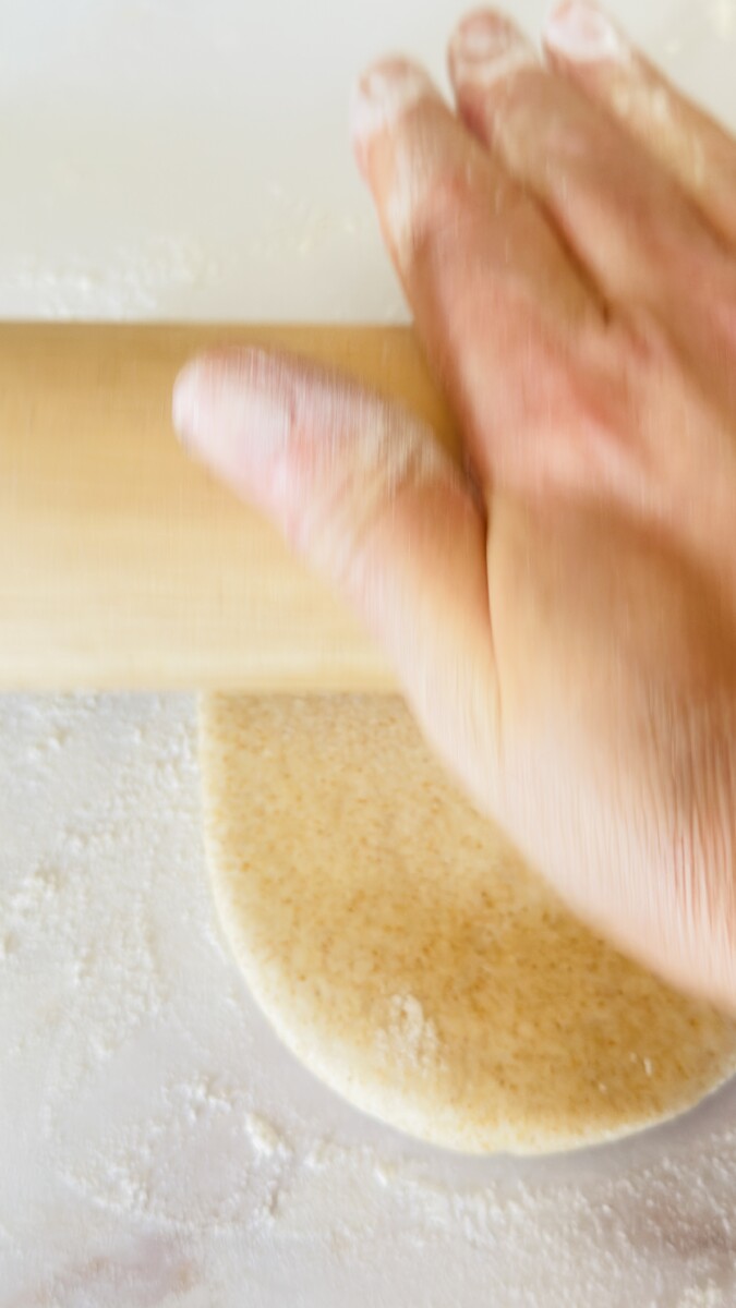 Rolling pita bread dough into a 6-inch wide circle on a floured surface.