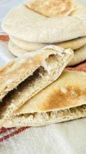 Stack of homemade pita bread with one cut in half to show the pocket inside.