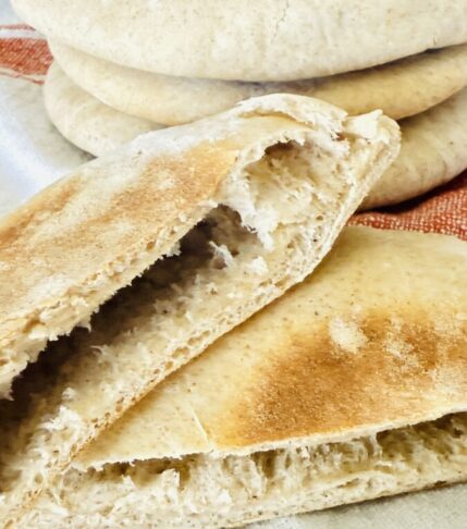 Stack of homemade pita bread with one cut in half to show the pocket inside.