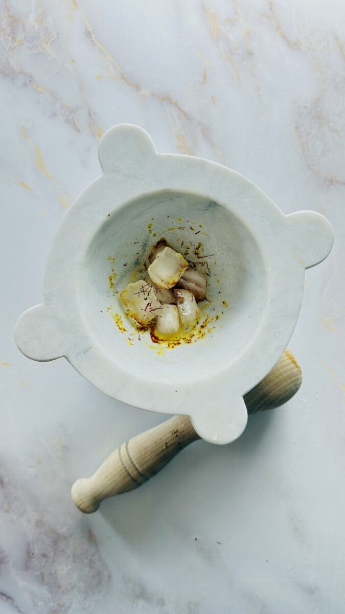 Crushed saffron threads in a mortar with melting ice cubes — traditional Moroccan ice method for making saffron water to use in fish tagine chermoula.