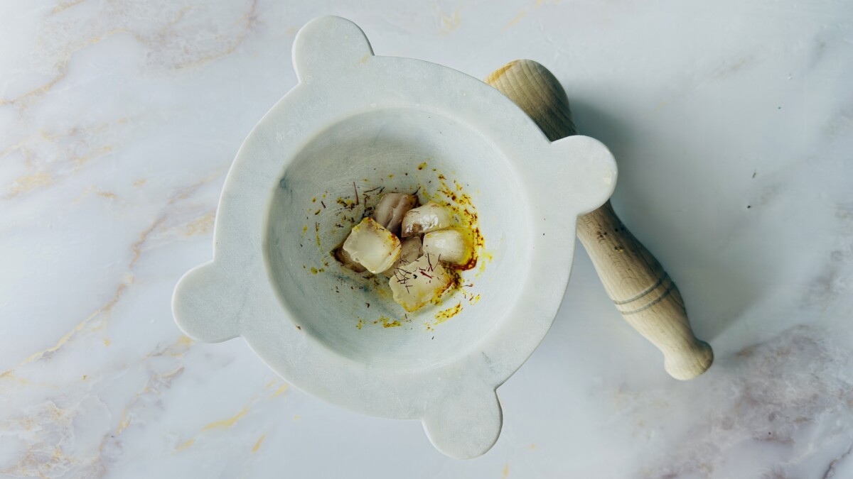 Crushed saffron threads in a mortar with melting ice cubes — traditional Moroccan ice method for making saffron water to use in fish tagine chermoula.