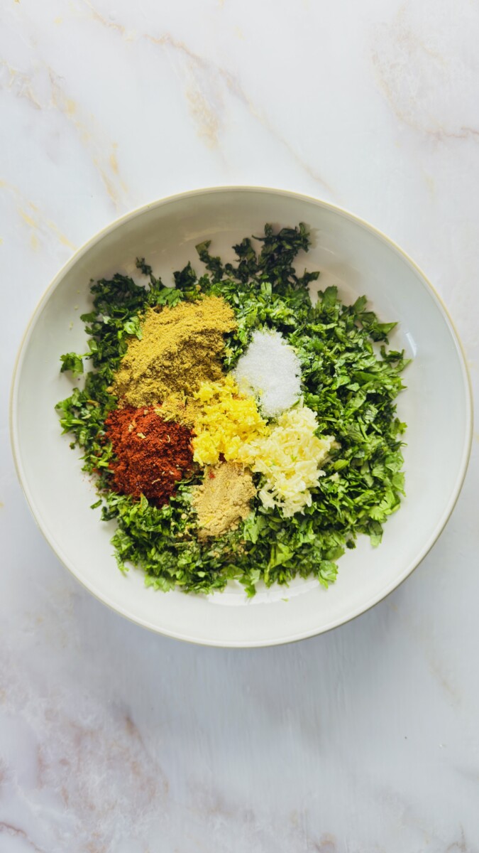 Fresh ingredients for Moroccan chermoula in a bowl — chopped cilantro, minced garlic, spices, saffron water, olive oil, lemon zest, and juice before mixing for the fish tagine.