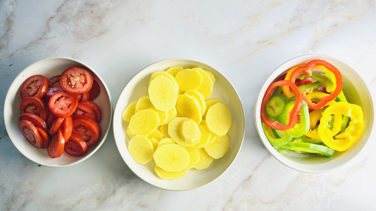 Fresh vegetables prepared for Moroccan Fish Tagine — sliced potatoes, Roma tomatoes, and colorful bell peppers ready to layer with chermoula and fish.