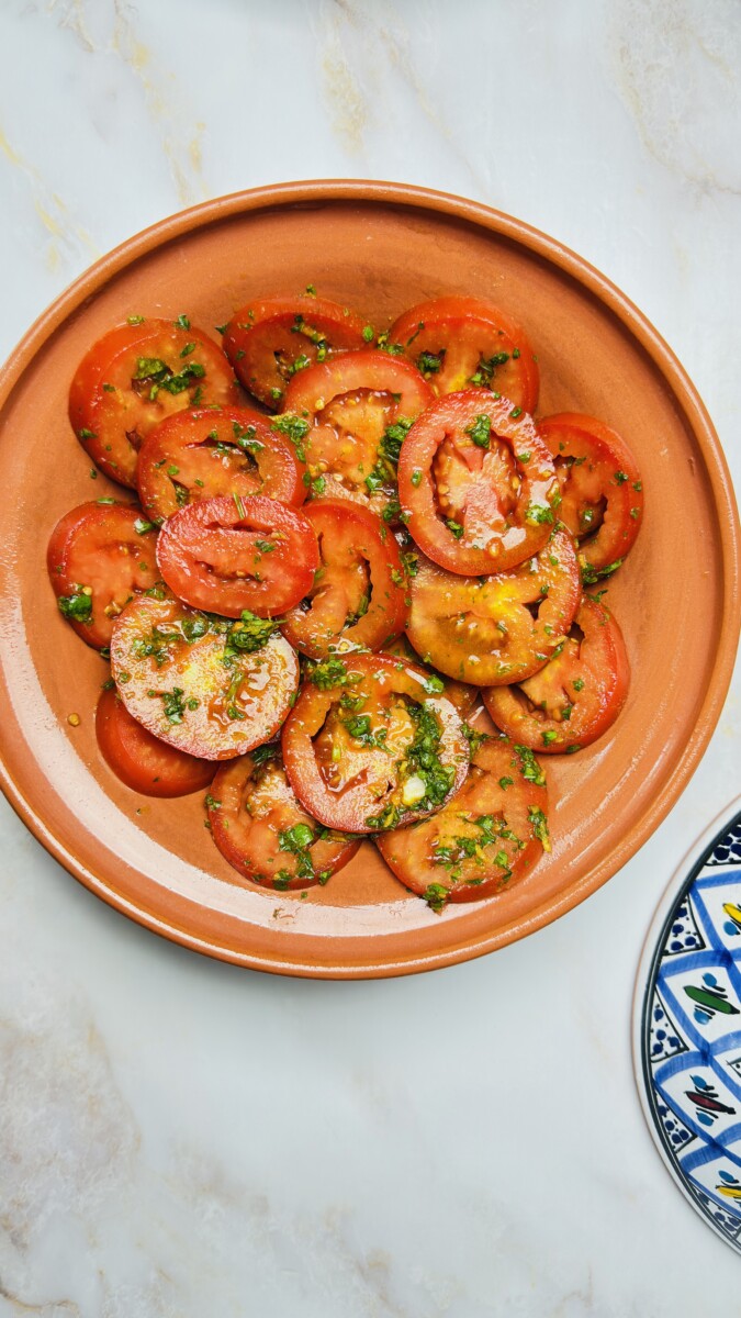 First layer of sliced Roma tomatoes arranged in the tagine base — starting the Moroccan Fish Tagine with a colorful, juicy foundation.