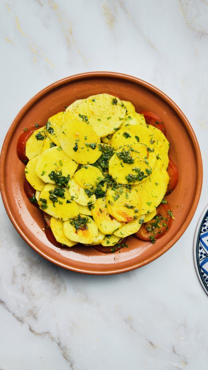 Thinly sliced yellow potatoes layered over tomatoes in the tagine — coated with chermoula for flavor and even cooking.