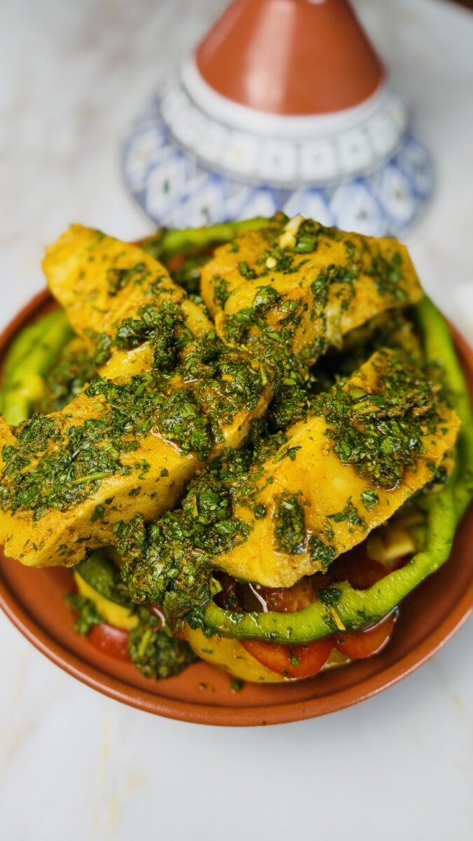 Marinated fish fillets placed on top of the layered vegetables in the tagine, with extra chermoula and lemon slices ready before cooking.