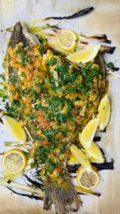 Whole baked Petrale sole topped with cherry tomato-caper sauce and garnished with fresh parsley, ready to serve.