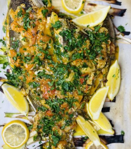 Whole baked Petrale sole topped with cherry tomato-caper sauce and garnished with fresh parsley, ready to serve.