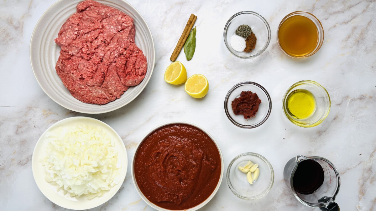 Ingredients for Greek Pastitsio meat sauce — ground beef, lamb, onions, garlic, tomatoes, and warm Mediterranean spices.