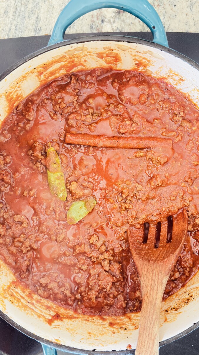 Adding crushed tomatoes, tomato paste, and warm Mediterranean spices to the Greek Pastitsio meat sauce.