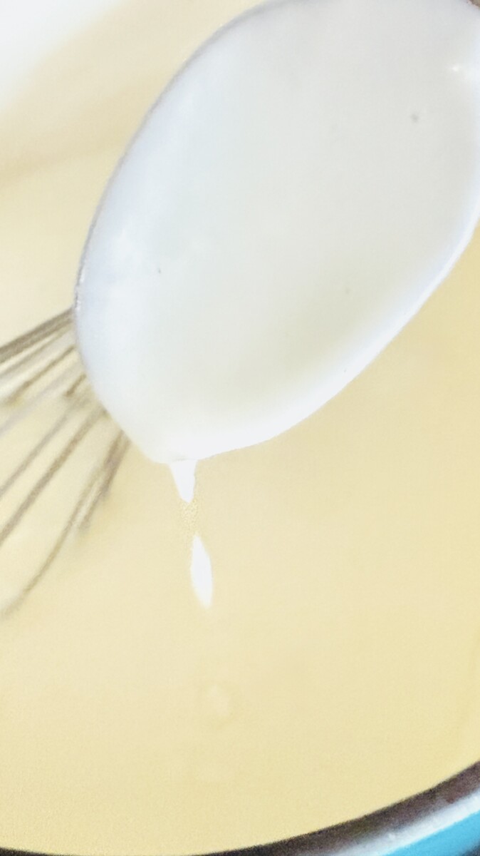 Whisking warm milk into the roux to create a smooth, creamy béchamel sauce for Greek Pastitsio.