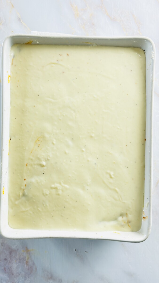 Pouring smooth béchamel sauce over the meat layer to finish assembling the Greek Pastitsio.