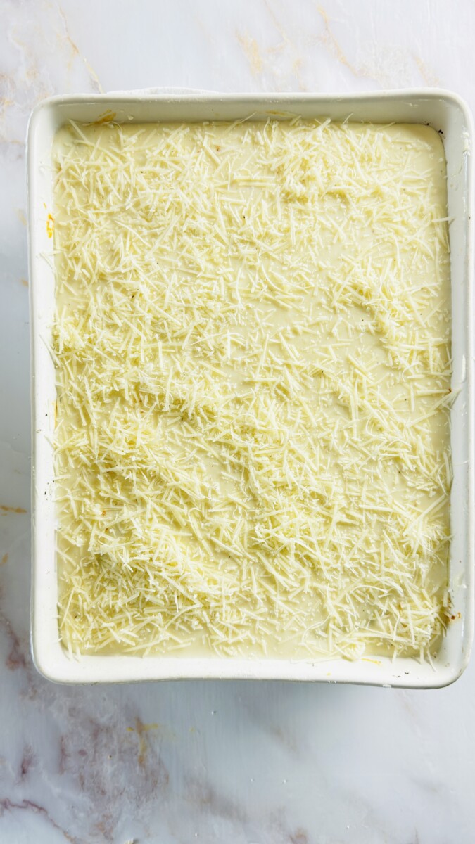 Sprinkling grated kefalotyri cheese over the béchamel before baking the Greek Pastitsio until golden.