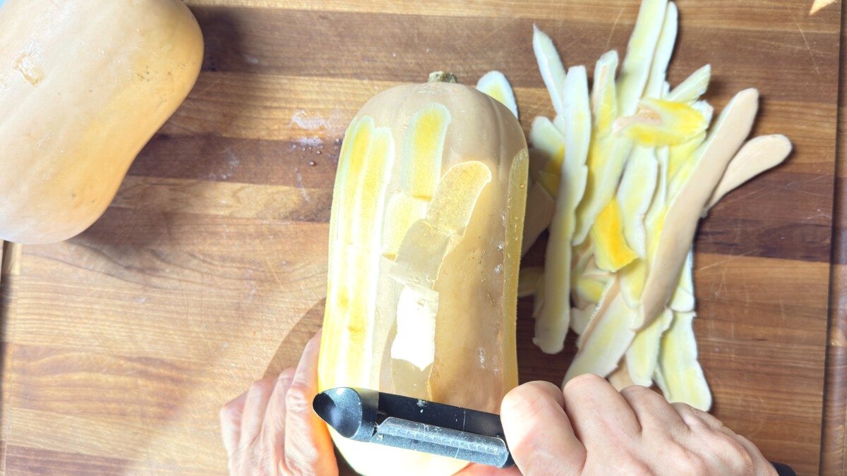 Peeling butternut squash with a vegetable peeler on cutting board