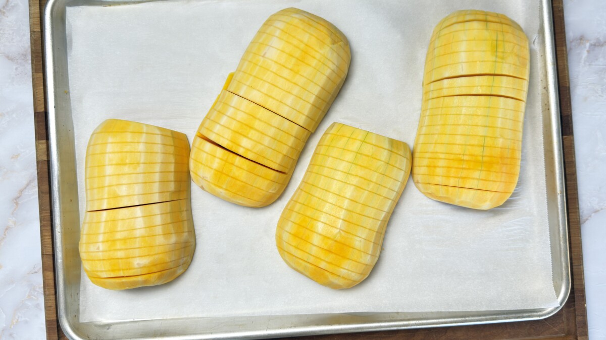 Four hasselback butternut squash halves arranged on parchment-lined baking sheet