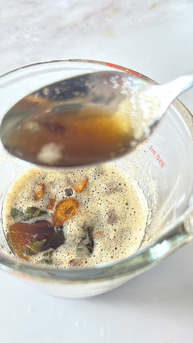 Spoonful of golden sage brown butter held over measuring cup showing nutty color