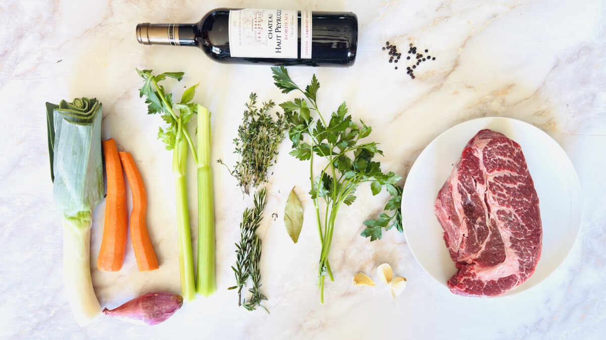  Alt Text: Ingredients for Beef Bourguignon including chuck beef, red wine, carrots, mushrooms, pearl onions, herbs, and spices arranged on a counter