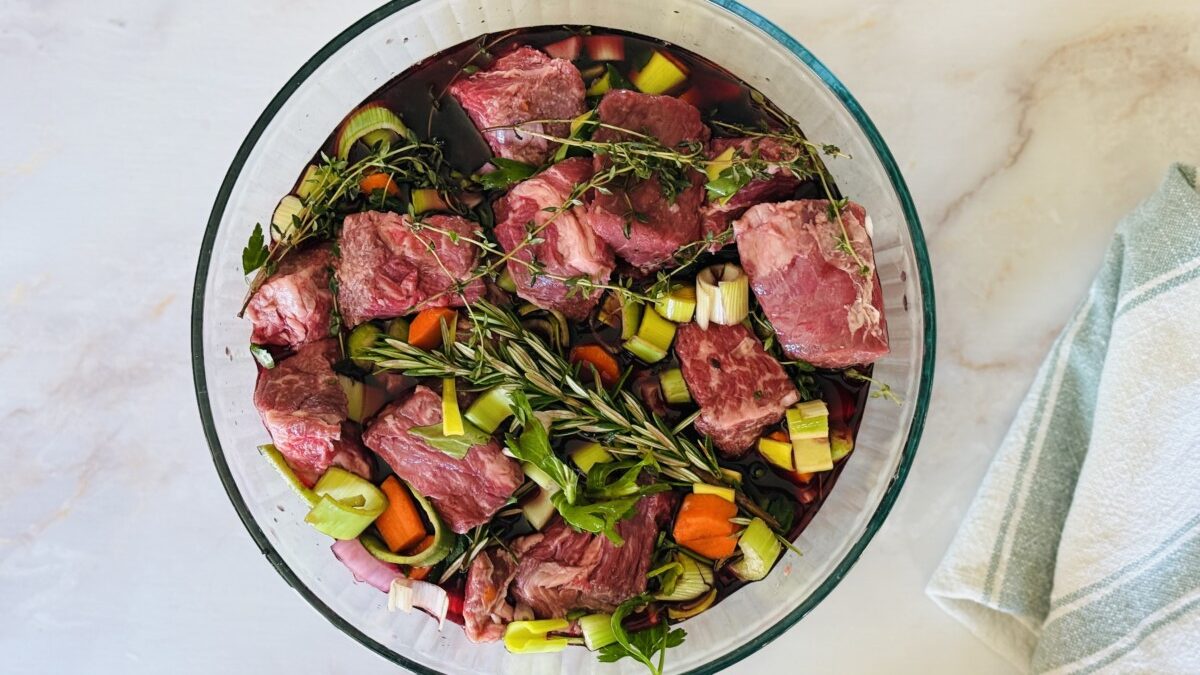Chuck beef cubes marinating in red wine with vegetables and herbs in a glass bowl