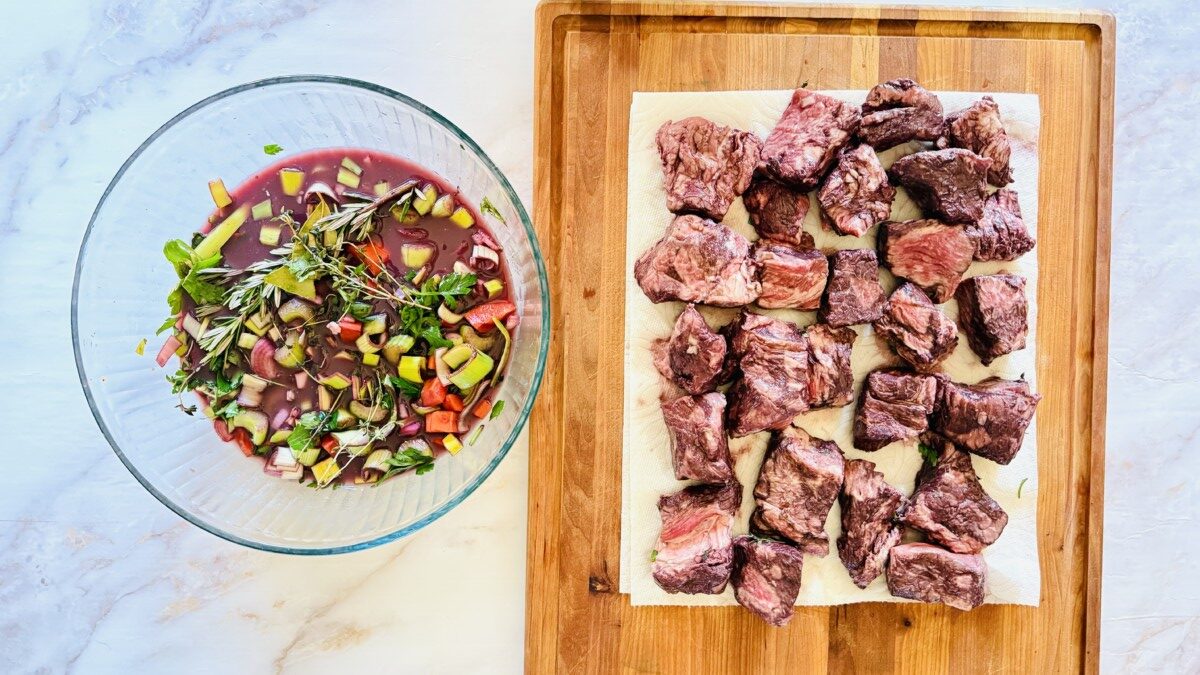 Dried beef cubes ready for searing with strained wine marinade in bowl on the side