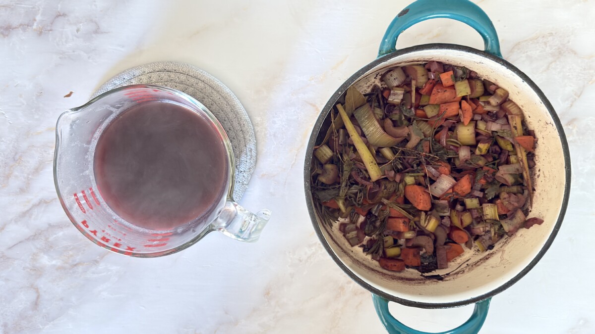 Straining cooked wine marinade through a fine mesh sieve to separate liquid from vegetables and herbs