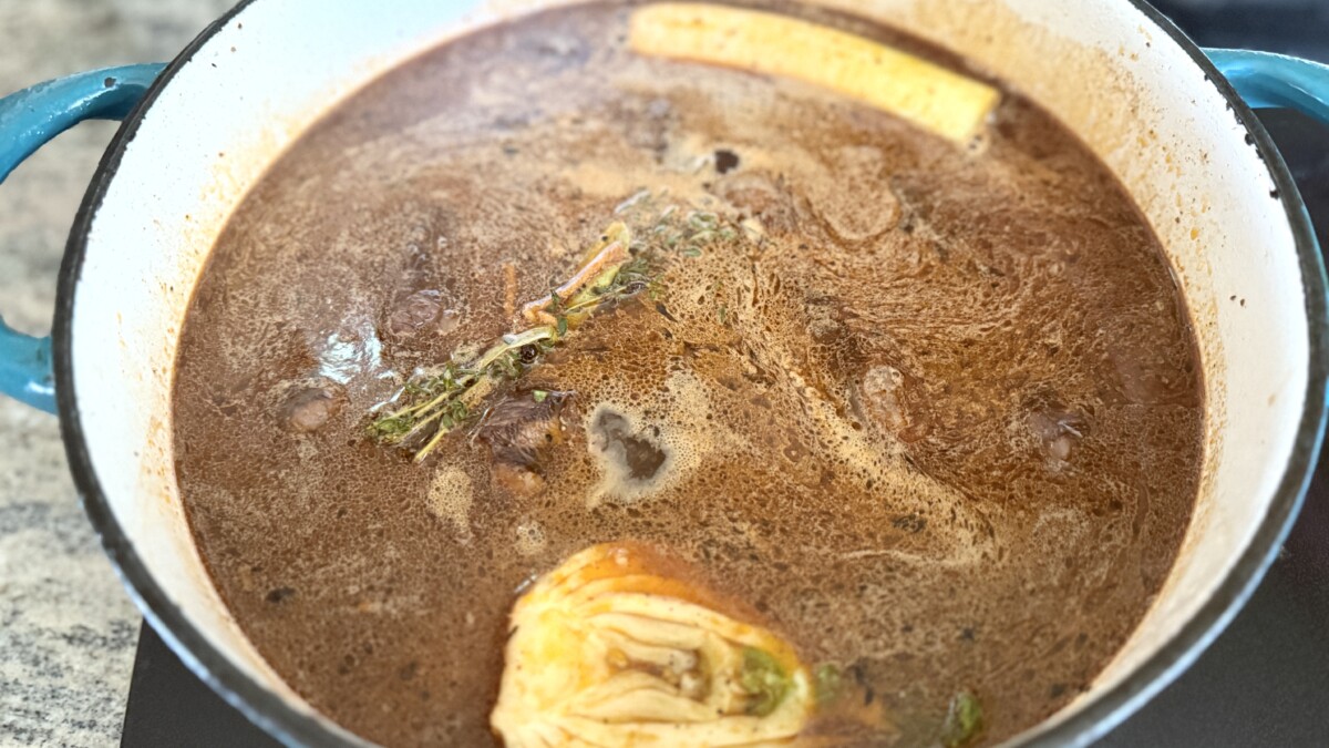 Seared beef in Dutch oven with beef broth, wine, and fresh herbs ready to braise