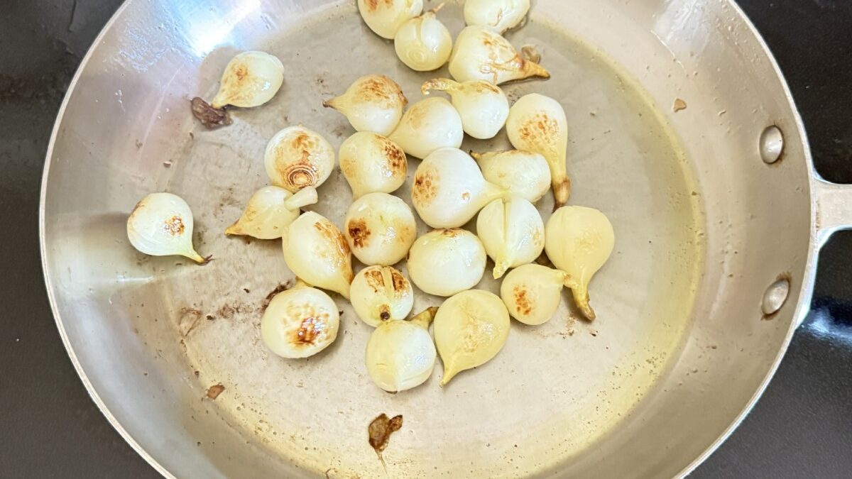 Pearl onions cooking in rendered pancetta fat until golden brown in a skillet