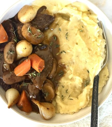 Beef Bourguignon with tender beef, mushrooms, and pearl onions in rich wine sauce served over creamy mashed potatoes