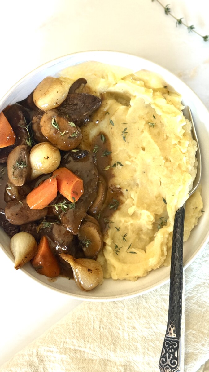 Beef Bourguignon with tender beef, mushrooms, and pearl onions in rich wine sauce served over creamy mashed potatoes