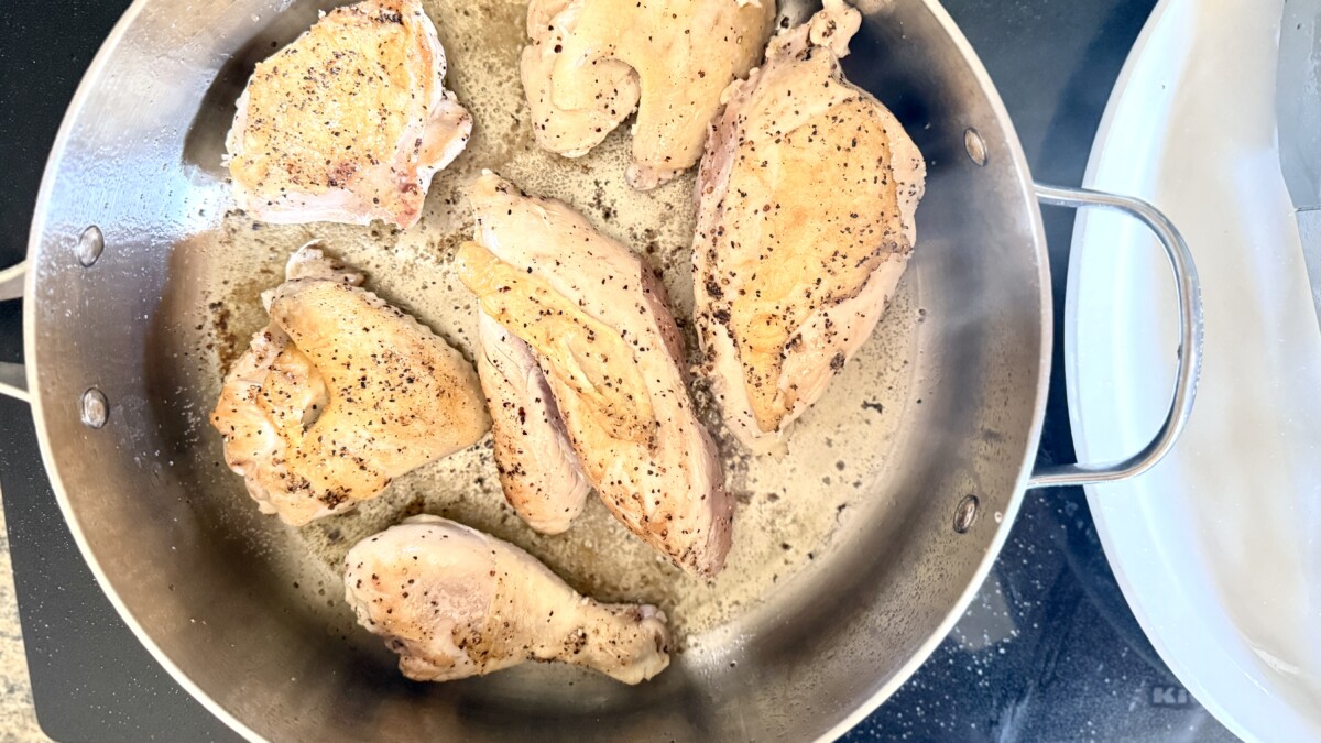 Golden brown chicken thighs being seared in a Dutch oven for chicken cacciatore