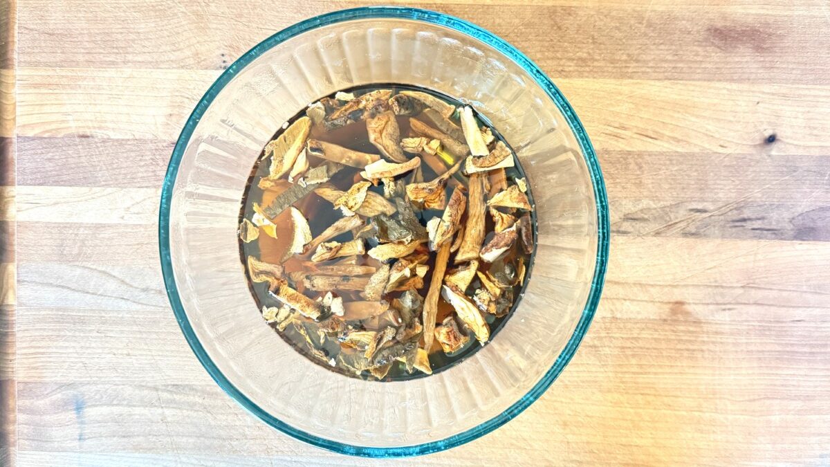 Dried porcini mushrooms soaking in hot water in a glass bowl for chicken cacciatore