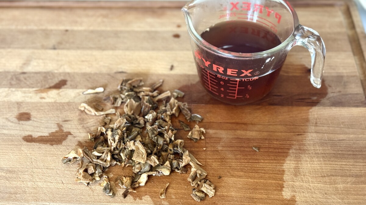 Rehydrated porcini mushrooms on a cutting board next to a measuring cup filled with strained mushroom soaking liquid for chicken cacciatore