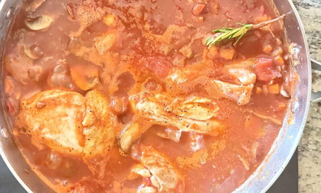 Chicken pieces braising in red wine tomato sauce with mushrooms in a partially covered Dutch oven