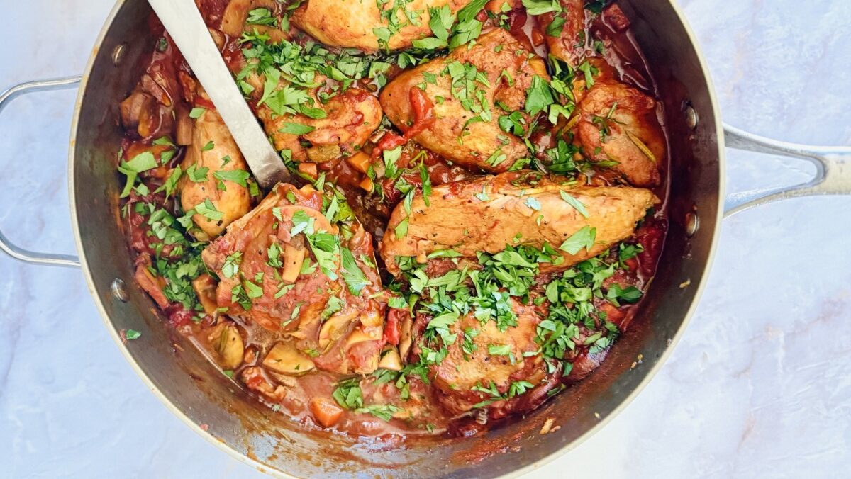 Authentic chicken cacciatore with porcini mushrooms in a rich red wine tomato sauce served in a Dutch oven with fresh parsley garnish