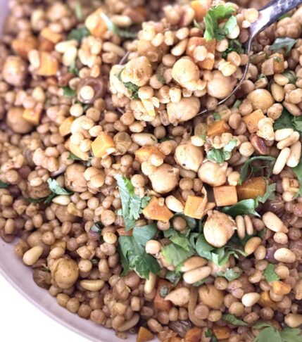 Pearl couscous recipe with chickpeas, carrots, golden raisins, and toasted pine nuts garnished with fresh herbs