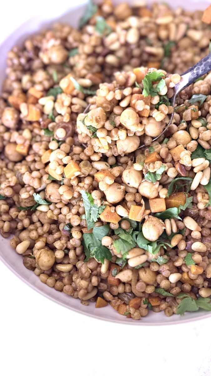Pearl couscous recipe with chickpeas, carrots, golden raisins, and toasted pine nuts garnished with fresh herbs