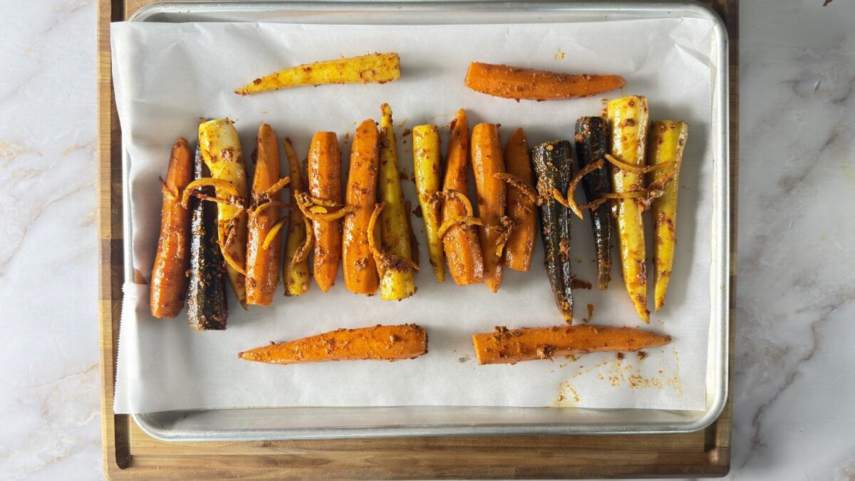 Rainbow carrots coated in harissa spice mixture arranged on a parchment-lined baking sheet ready to roast