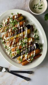 Harissa roasted carrots on a white platter drizzled with yogurt sauce and garnished with preserved lemon ribbons and fresh parsley