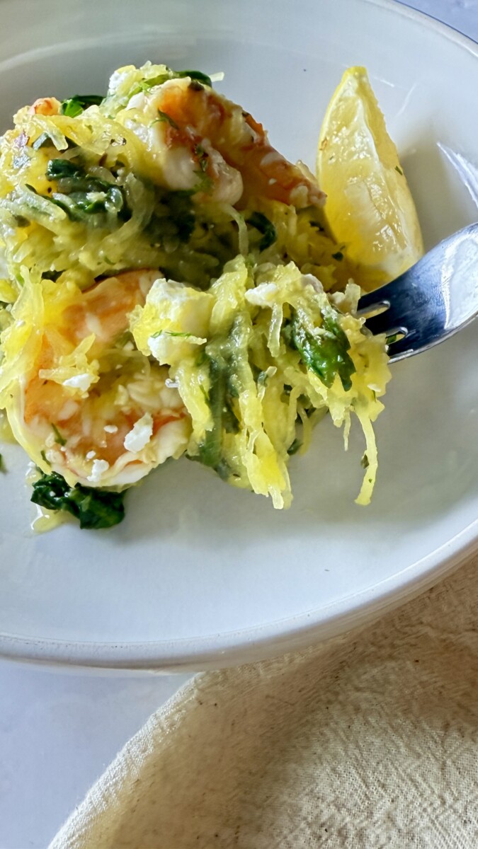 Mediterranean spaghetti squash with shrimp and feta served on a white plate with lemon wedges and fresh parsley